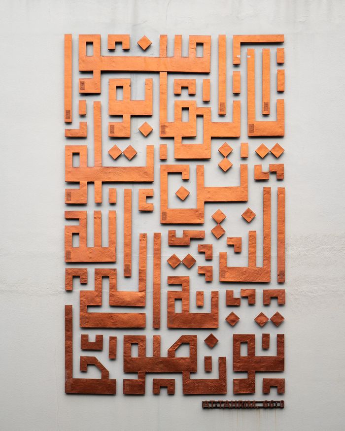 Copper Arabic calligraphy art in Kufic style on a wall in Jakarta, Indonesia.