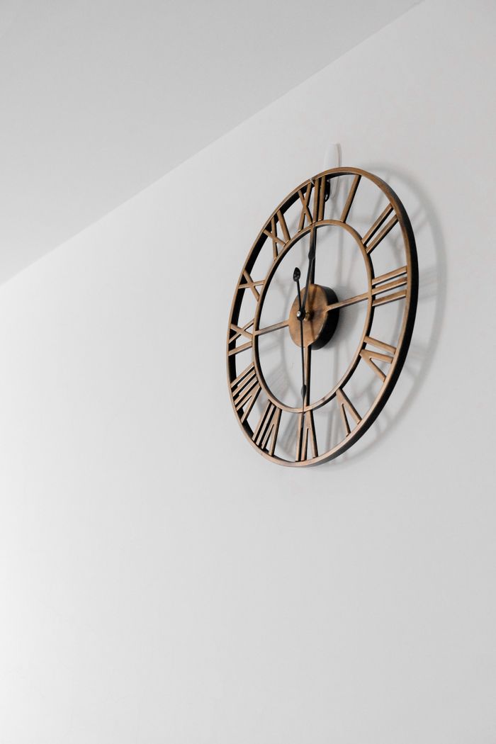 A stylish vintage wall clock with Roman numerals on a minimalist white wall.